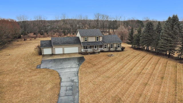 view of front of property with a wooded view, a front yard, covered porch, a garage, and driveway