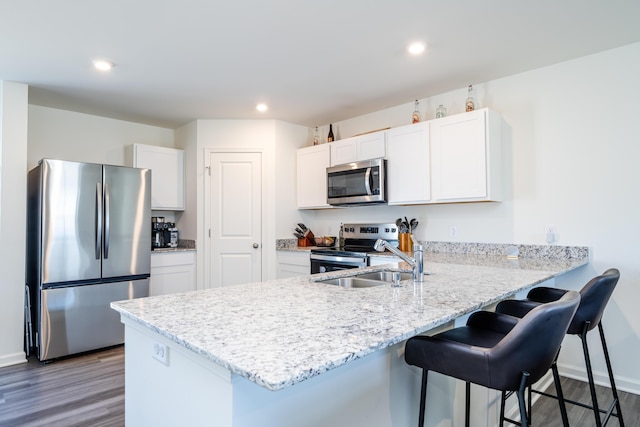 kitchen featuring a breakfast bar, appliances with stainless steel finishes, a peninsula, wood finished floors, and white cabinets