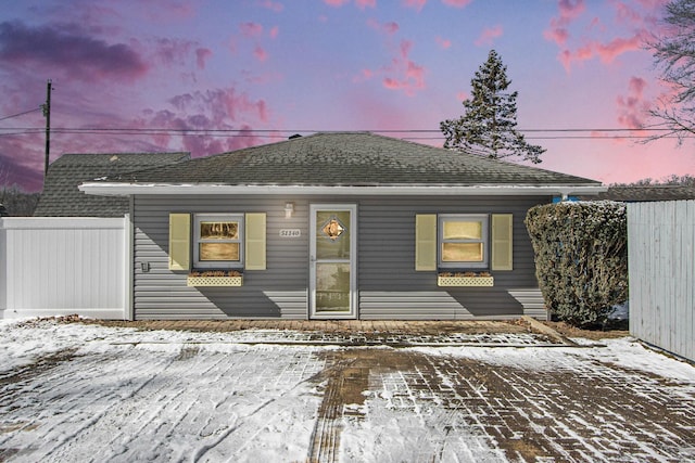 snow covered back of property featuring roof with shingles and fence