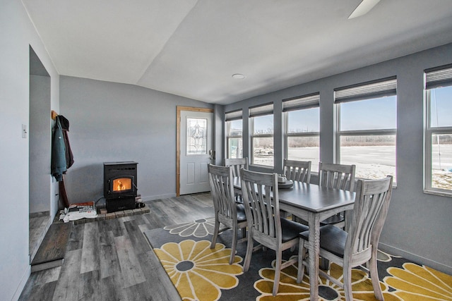 dining area with vaulted ceiling, a wood stove, baseboards, and wood finished floors