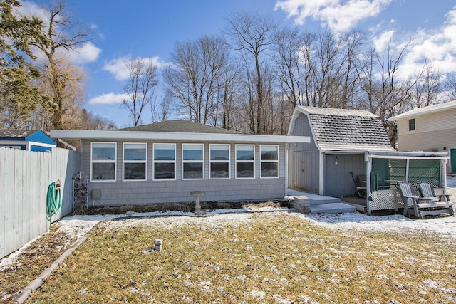 back of property featuring a yard, a gambrel roof, an outbuilding, and fence