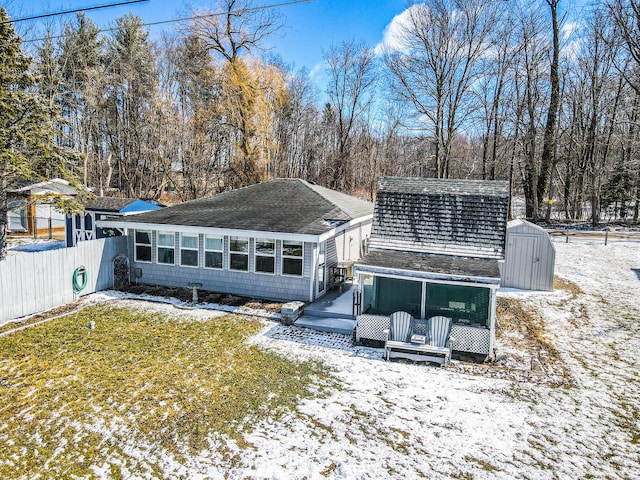 snow covered property featuring fence, a sunroom, an outdoor structure, a deck, and a storage shed