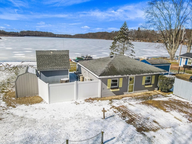 view of front of house with an outbuilding, a storage shed, roof with shingles, and fence