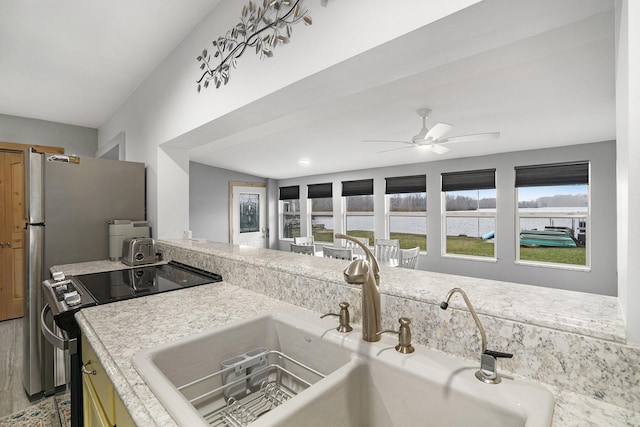 kitchen with a sink, ceiling fan, light countertops, a water view, and range with electric stovetop
