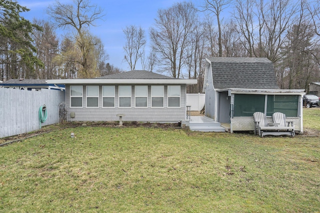 back of house with a sunroom, a yard, a shingled roof, and fence