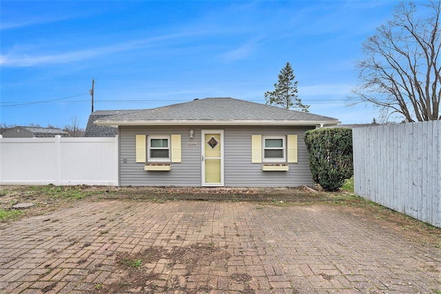 view of front facade featuring fence, roof with shingles, and a patio