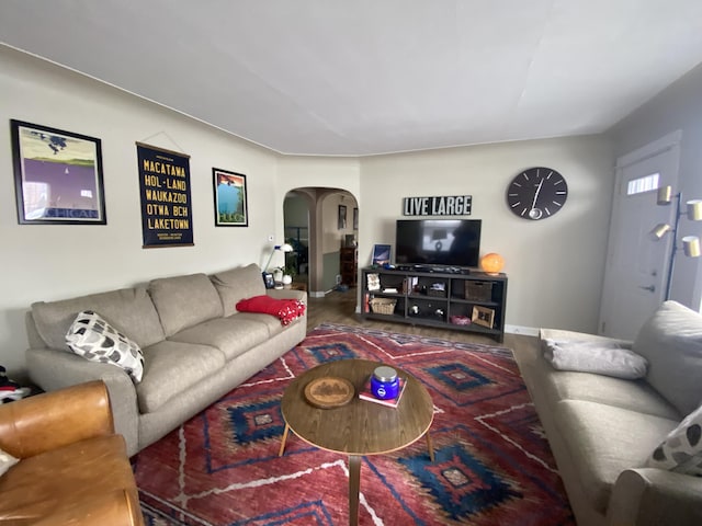 living room featuring wood finished floors, arched walkways, and baseboards