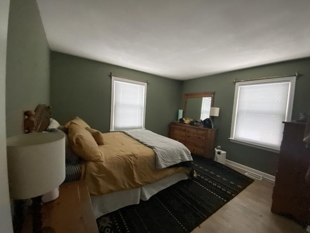 bedroom featuring visible vents, multiple windows, baseboards, and wood finished floors