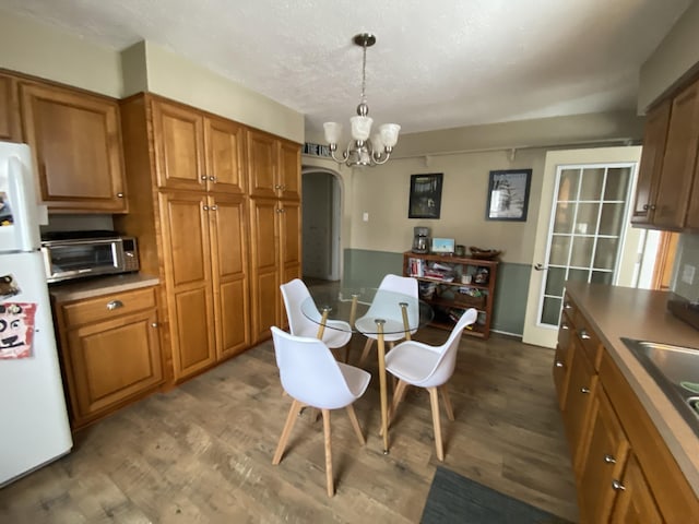 kitchen featuring dark wood-style floors, brown cabinetry, arched walkways, freestanding refrigerator, and a chandelier