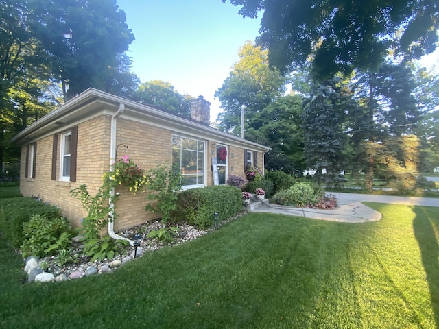 view of home's exterior with brick siding, a lawn, and a chimney