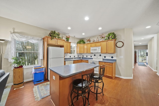 kitchen with a center island, baseboards, a kitchen breakfast bar, light wood-style floors, and white appliances