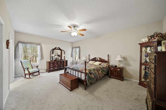 bedroom featuring a textured ceiling, light colored carpet, baseboards, and ceiling fan