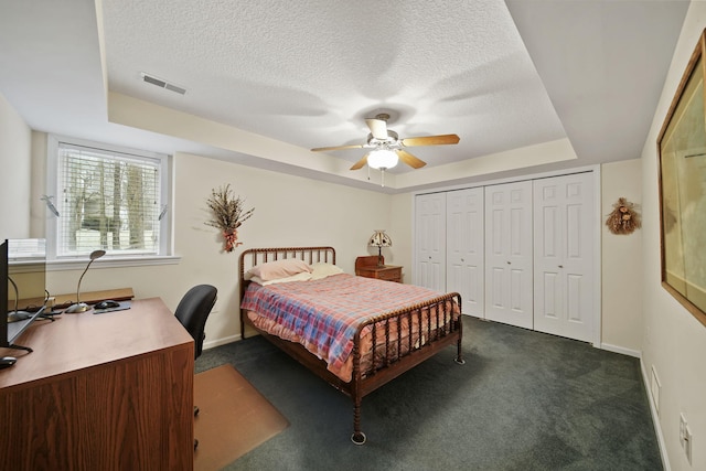 bedroom featuring visible vents, a textured ceiling, a raised ceiling, and dark colored carpet