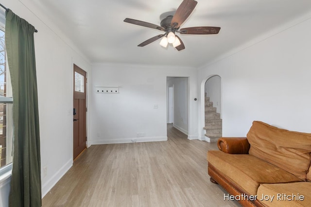 unfurnished room with baseboards, arched walkways, light wood-style flooring, and stairs