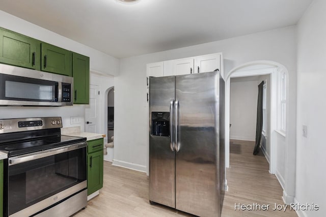 kitchen with green cabinets, light wood-style flooring, arched walkways, and appliances with stainless steel finishes