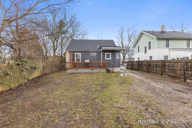 back of house with board and batten siding, a fenced backyard, a lawn, and a wooden deck