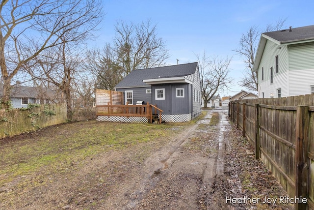 rear view of property with a yard, a fenced backyard, dirt driveway, a deck, and board and batten siding