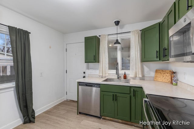 kitchen featuring green cabinetry, a sink, light countertops, light wood-style floors, and appliances with stainless steel finishes