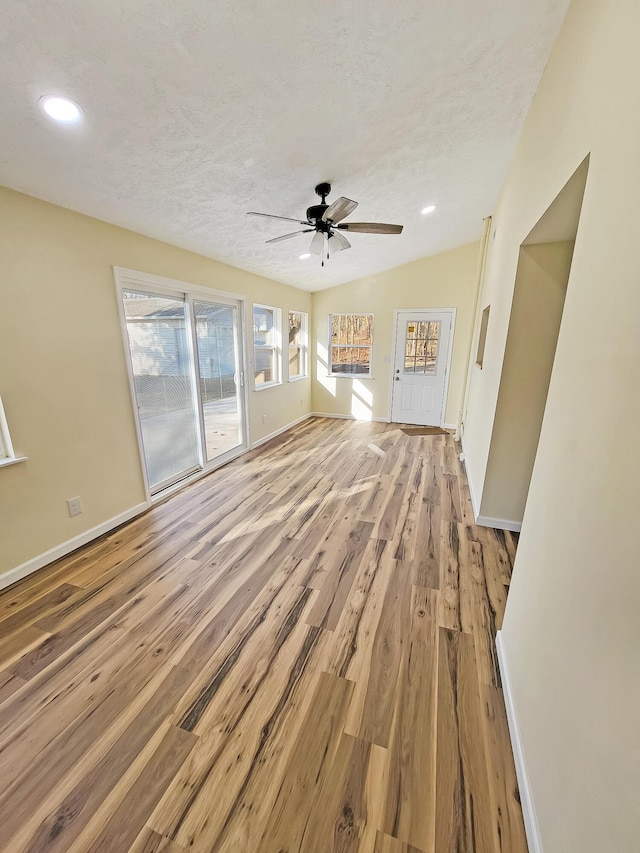 unfurnished living room with baseboards, ceiling fan, a textured ceiling, and light wood-style floors