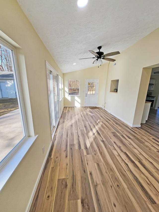 unfurnished living room featuring a healthy amount of sunlight, a textured ceiling, lofted ceiling, and wood finished floors