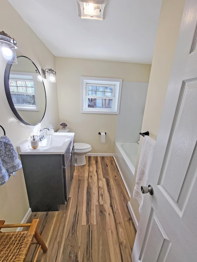 bathroom with vanity, wood finished floors, a tub to relax in, baseboards, and toilet