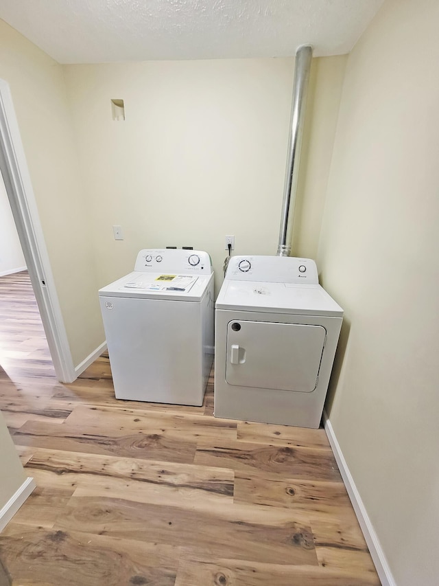 clothes washing area with baseboards, laundry area, light wood-style floors, washer and dryer, and a textured ceiling