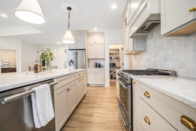 kitchen featuring light wood finished floors, decorative light fixtures, premium appliances, custom exhaust hood, and a sink