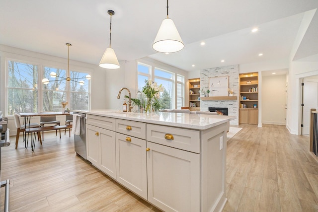 kitchen with stainless steel dishwasher, a brick fireplace, light wood-type flooring, and a wealth of natural light