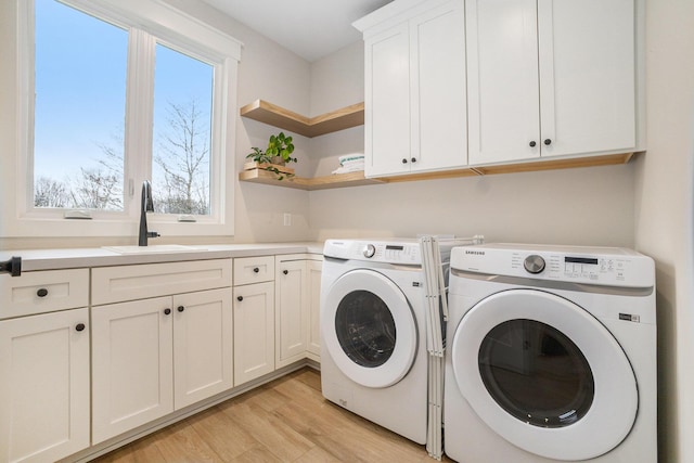 laundry room with a sink, cabinet space, light wood-style floors, and washing machine and clothes dryer