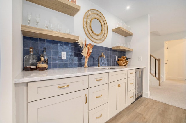 bar with beverage cooler, a sink, stairs, light wood-style floors, and tasteful backsplash