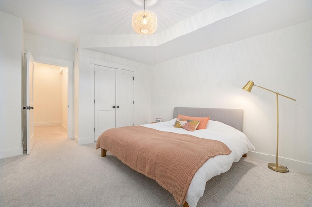 bedroom with a closet, baseboards, light colored carpet, and a raised ceiling