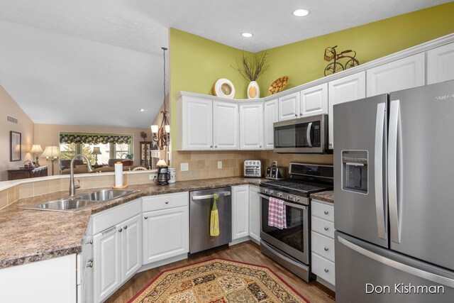 kitchen featuring a sink, stainless steel appliances, white cabinets, decorative backsplash, and lofted ceiling