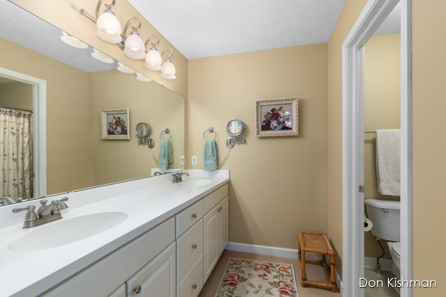 bathroom featuring double vanity, toilet, baseboards, and a sink