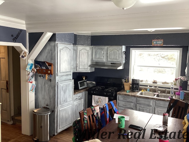 kitchen with dark wood-style floors, black gas range oven, ornamental molding, a sink, and under cabinet range hood