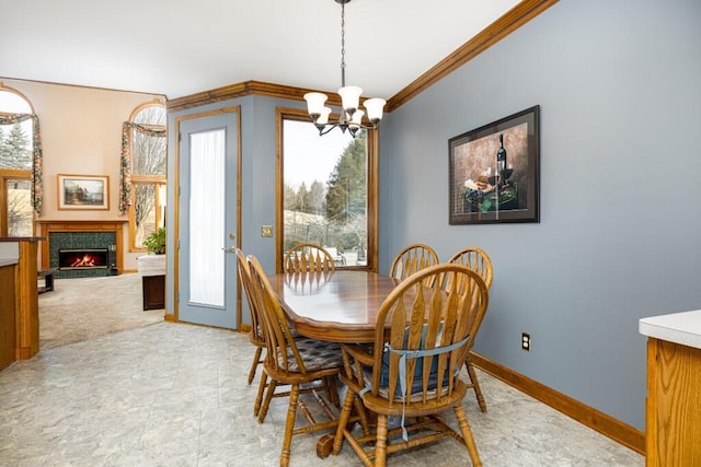 dining area featuring a lit fireplace, baseboards, an inviting chandelier, and ornamental molding