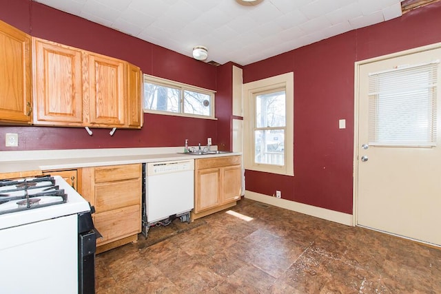 kitchen with light brown cabinetry, a sink, white appliances, light countertops, and baseboards