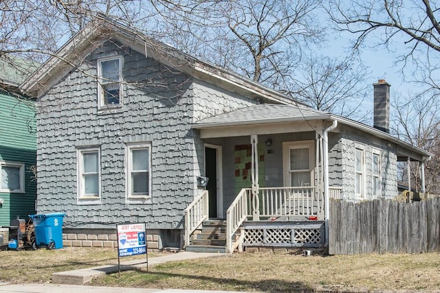 view of front of house featuring roof with shingles, a chimney, and fence