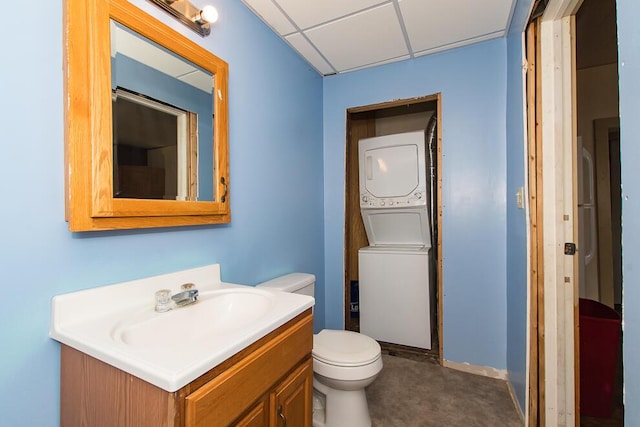 bathroom featuring a drop ceiling, toilet, vanity, and stacked washer and dryer