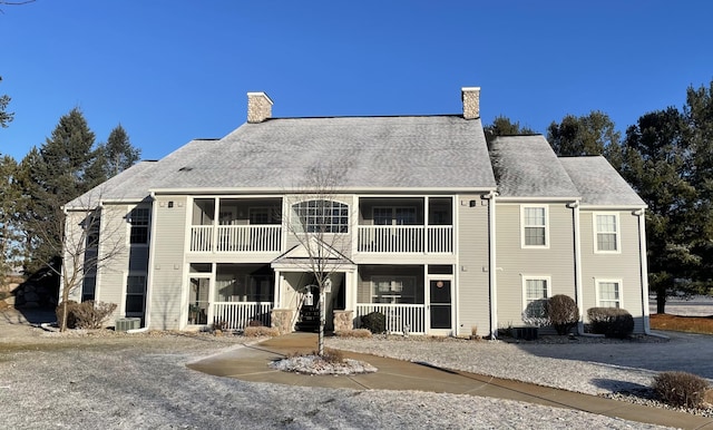 back of property with cooling unit, roof with shingles, and a chimney