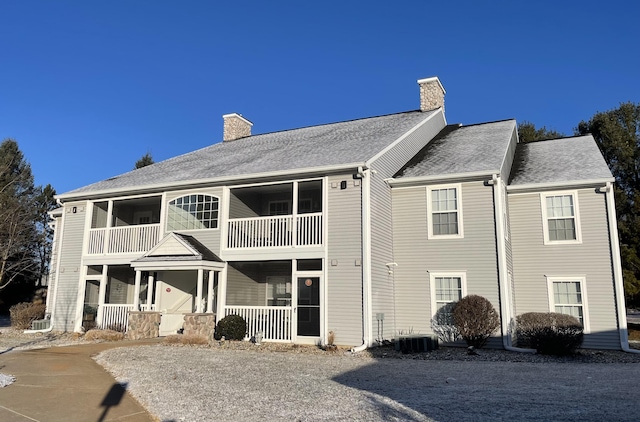 rear view of house with central air condition unit, a balcony, covered porch, and a chimney