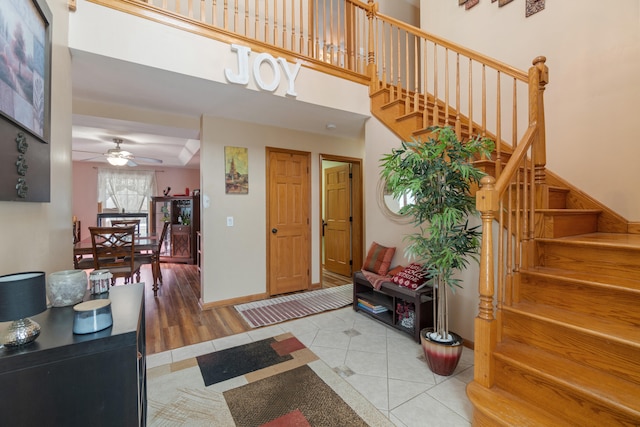 tiled foyer featuring baseboards, stairs, a ceiling fan, and a towering ceiling