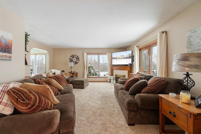 carpeted living room with arched walkways and a lit fireplace