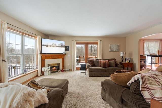 living room featuring baseboards, arched walkways, carpet, and a glass covered fireplace