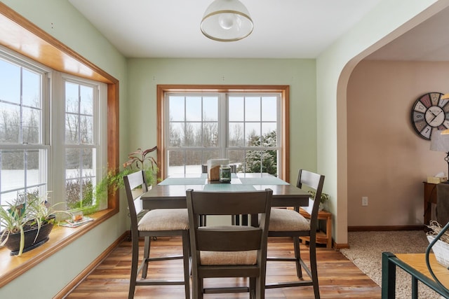 dining area featuring baseboards, arched walkways, and light wood-type flooring