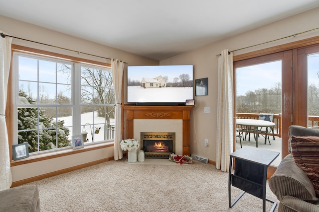 carpeted living room featuring visible vents, baseboards, and a lit fireplace