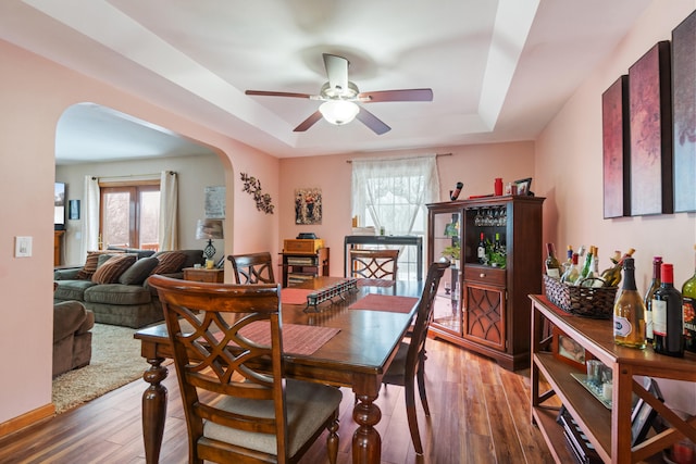 dining room with a ceiling fan, a tray ceiling, wood finished floors, and arched walkways