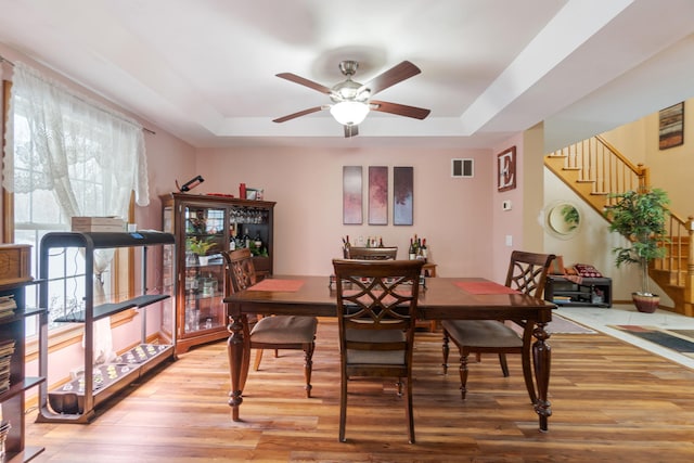 dining area with a tray ceiling, visible vents, and light wood finished floors