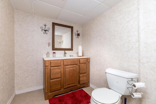 bathroom featuring vanity, baseboards, a drop ceiling, tile patterned floors, and toilet