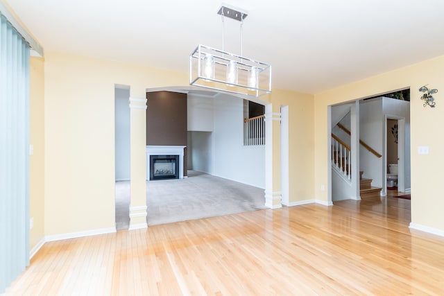 unfurnished living room with light wood finished floors, a fireplace, stairs, and decorative columns