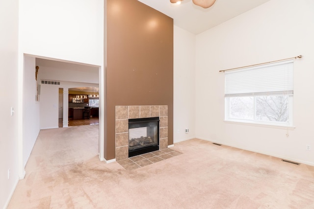 unfurnished living room featuring visible vents, carpet floors, a high ceiling, and a fireplace